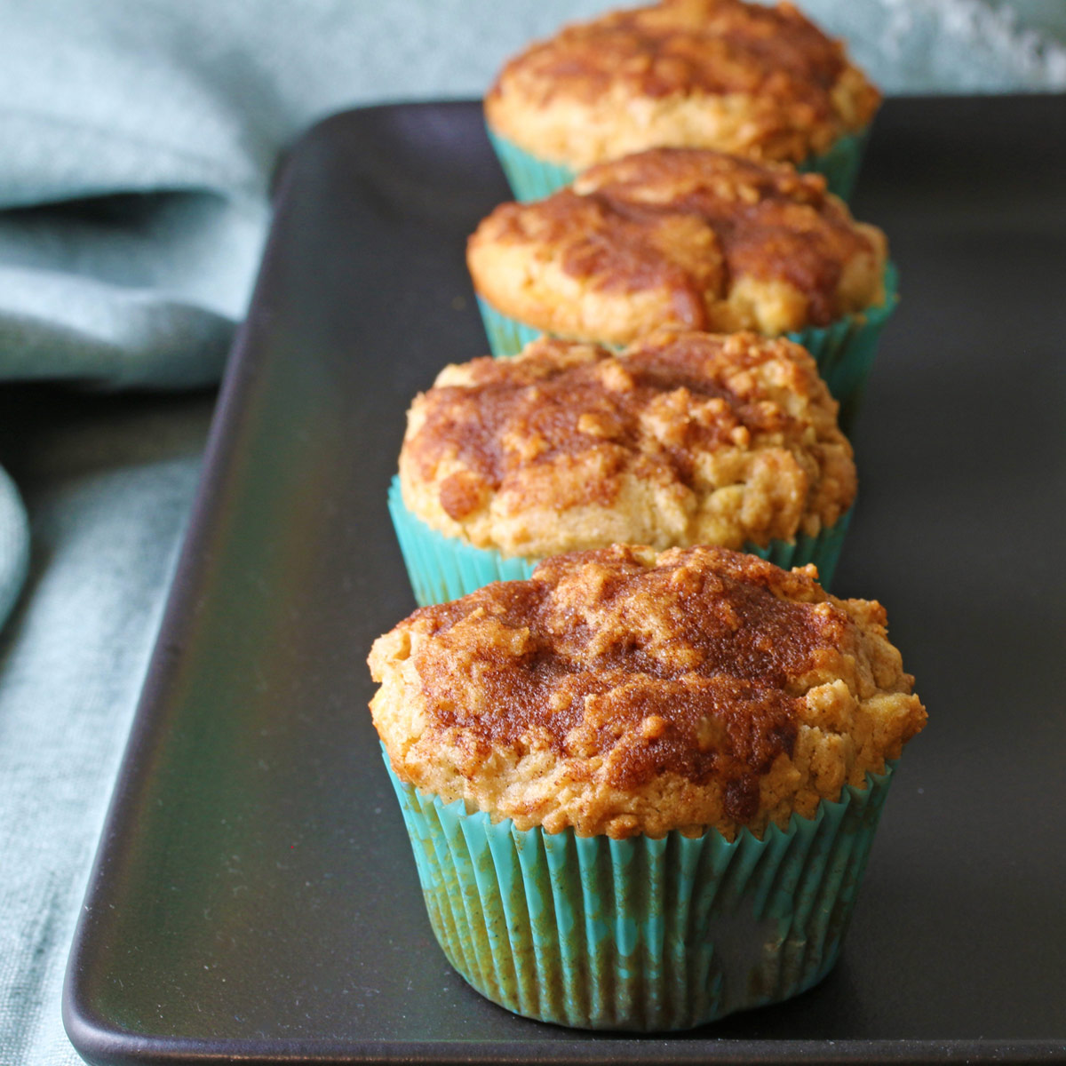 Snickerdoodle Muffins with White Chocolate lined up on a black tray with an aqua colored cloth around it © 2024 Jane Bonacci, The Heritage Cook.