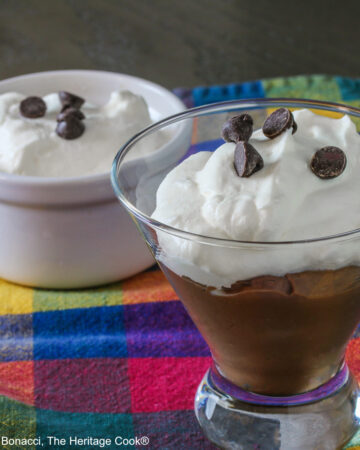 Homemade Nutella Pudding in white ramekins and clear glass containers with whipped cream on top and sprinkled with chocolate chips on brightly colored plaid cloth © 2024 Jane Bonacci, The Heritage Cook.