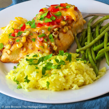 Large chicken breast topped with melted cheese, sauteed onions, bell peppers, poblano peppers, and garlic, garnished with chopped parsley and red bell peppers. Served with yellow rice and green beans © 2024 Jane Bonacci, The Heritage Cook.