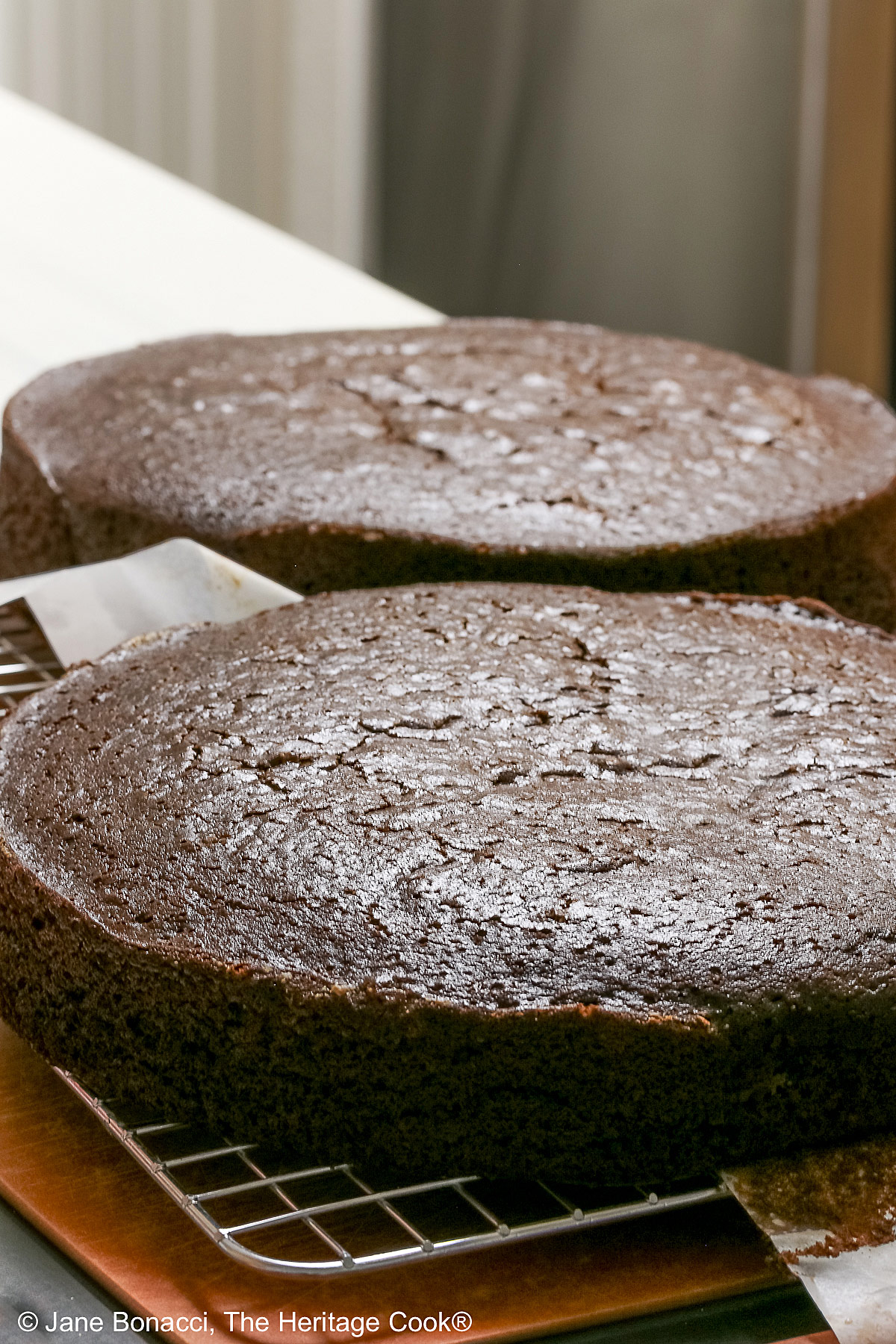 Two baked chocolate cake layers, cooling on a wire rack. 
