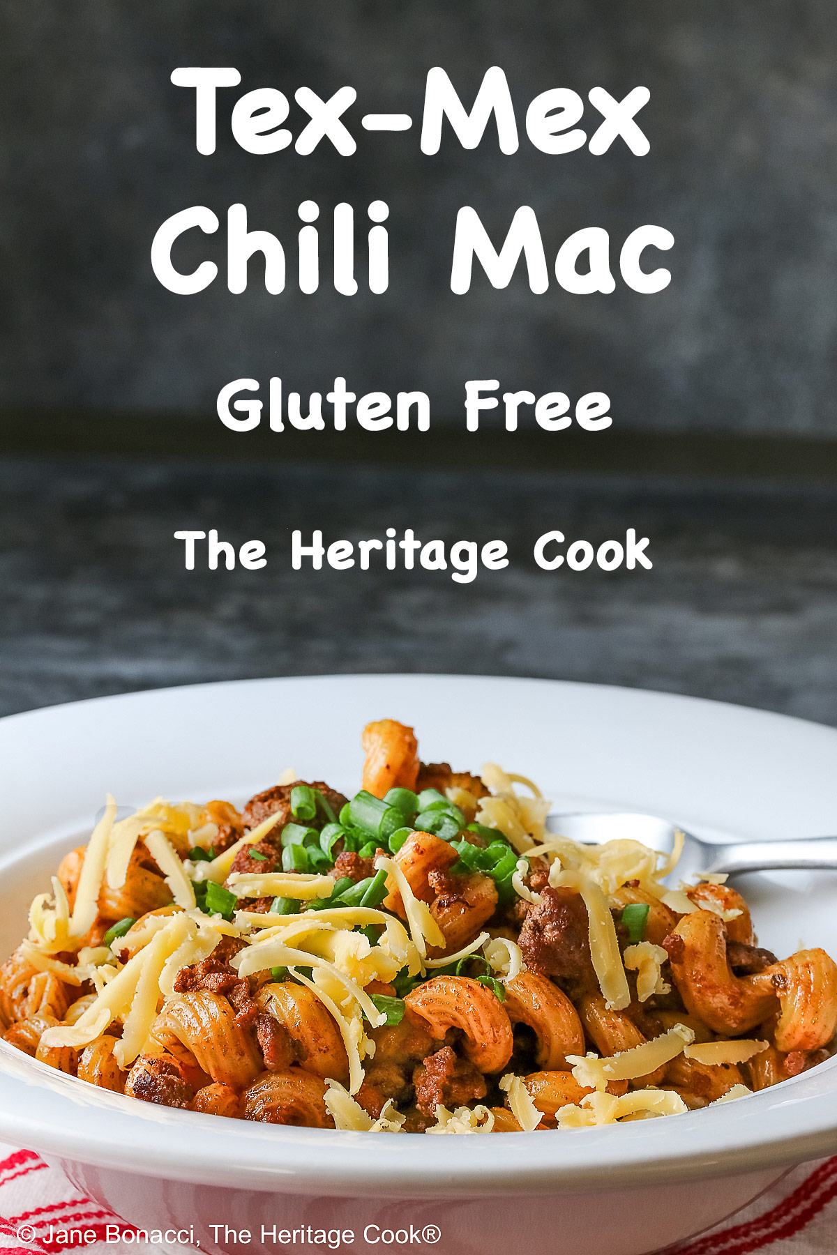 Tex-Mex Chili Mac made in the Instant Pot scooped into a white bowl with a wide rim, topped with chopped chives and extra shredded cheese, sitting on a red and white striped cloth © 2025 Jane Bonacci, The Heritage Cook.