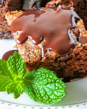 3 squares of Egg-Free Chocolate, Chocolate Chip Cake on a white plate with a couple of sprigs of mint, sitting on a brightly colored plaid cloth © 2025 Jane Bonacci, The Heritage Cook.