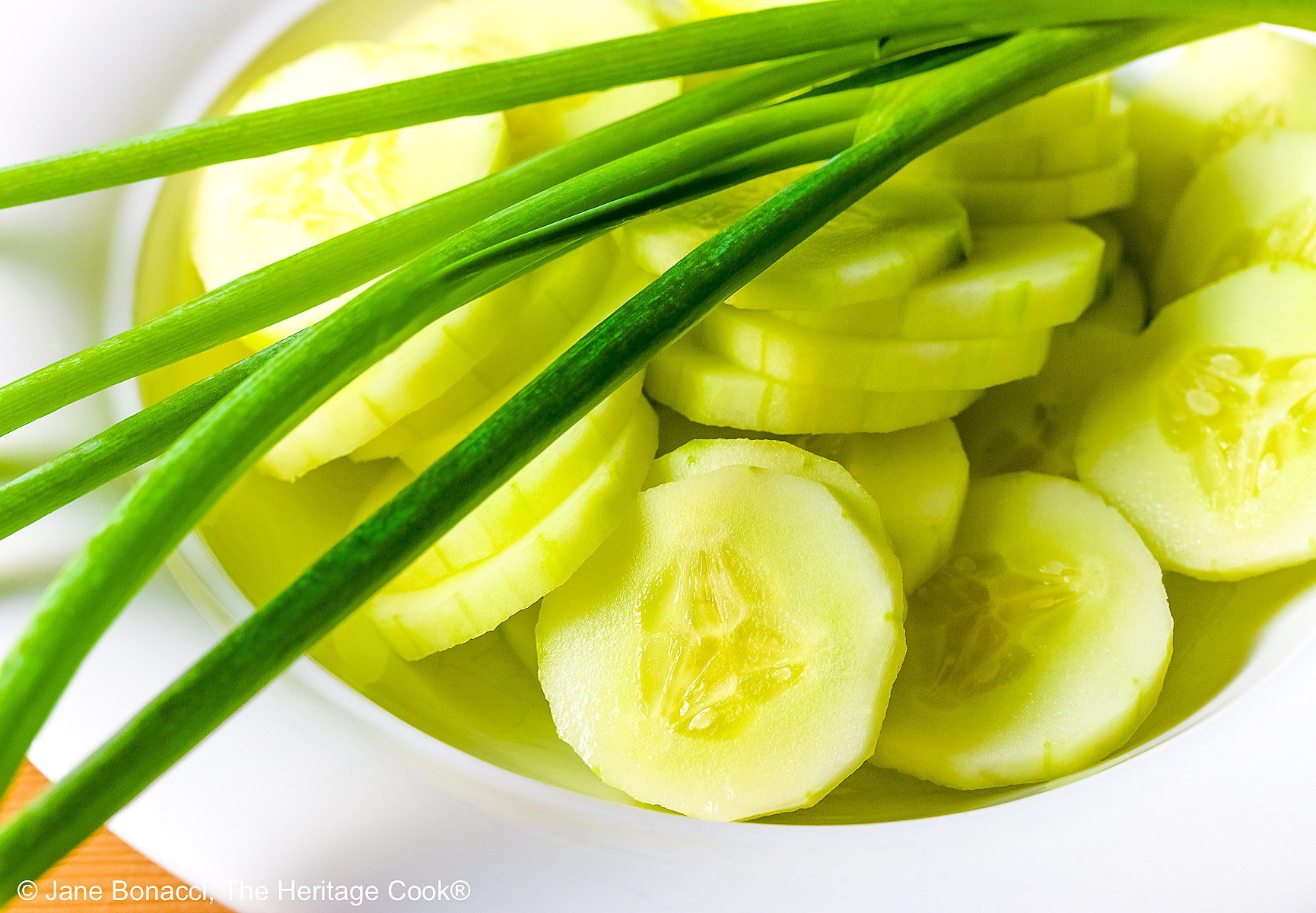 Concentric circles of tomatoes and cucumbers, each ring alternating between the two vegetables, drizzled with homemade vinaigrette and sprinkled with chopped green onions on a white plate © 2025 Jane Bonacci, The Heritage Cook. 