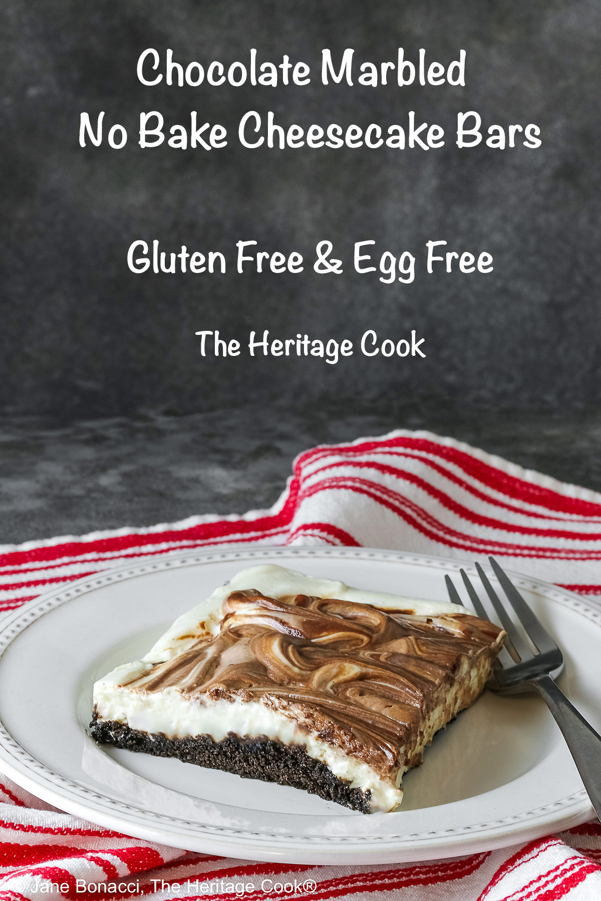 Square slice of Marbled No-Bake Cheesecake Bars on a white plate with a fork alongside, sitting on a red and white cloth on a dark gray background © 2025 Jane Bonacci, The Heritage Cook.