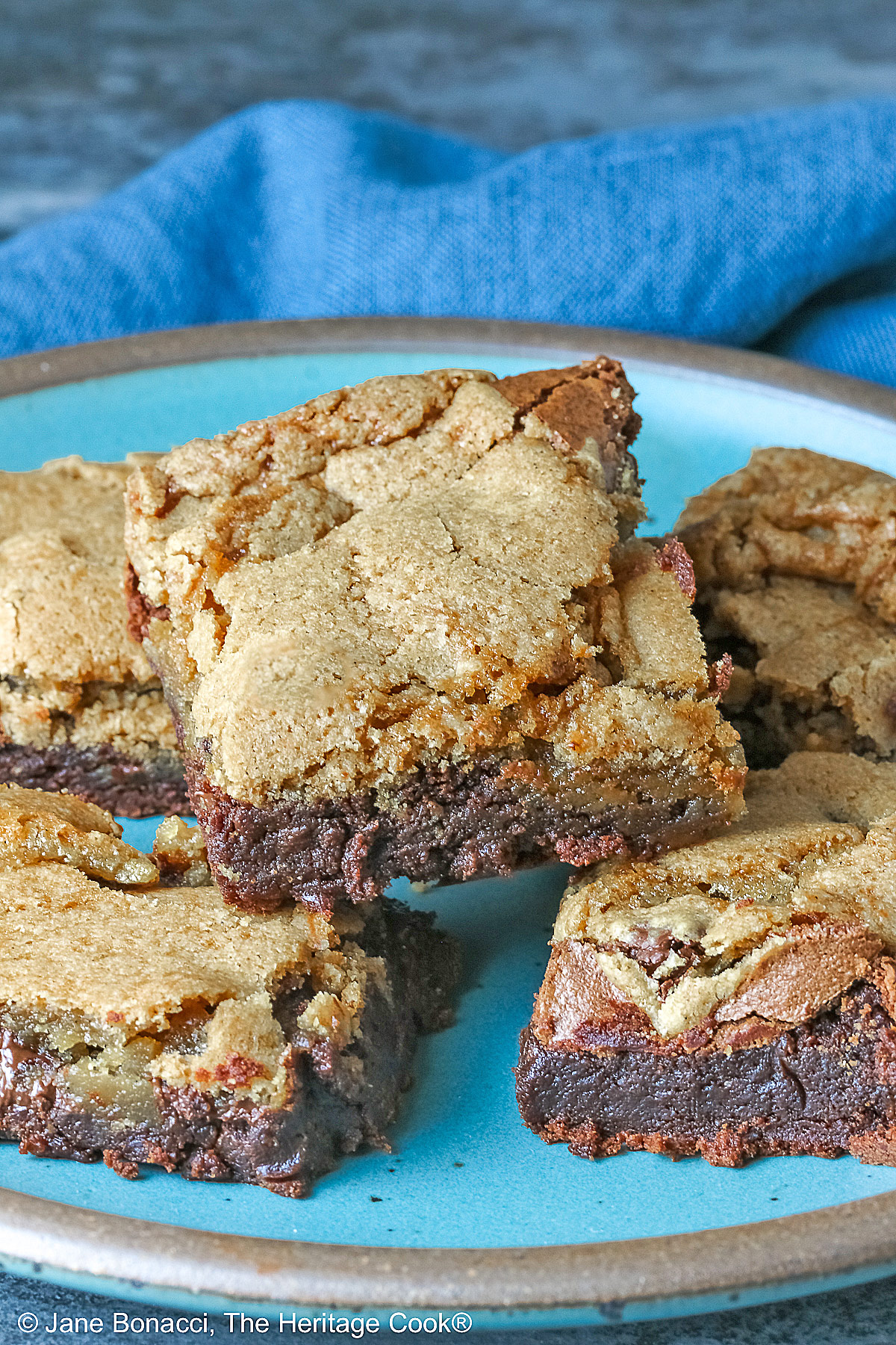 5 stacked Double Chocolate Brookies sitting on a turquoise colored plate with a medium blue cloth behind, on a mottled gray background © 2025 Jane Bonacci, The Heritage Cook.