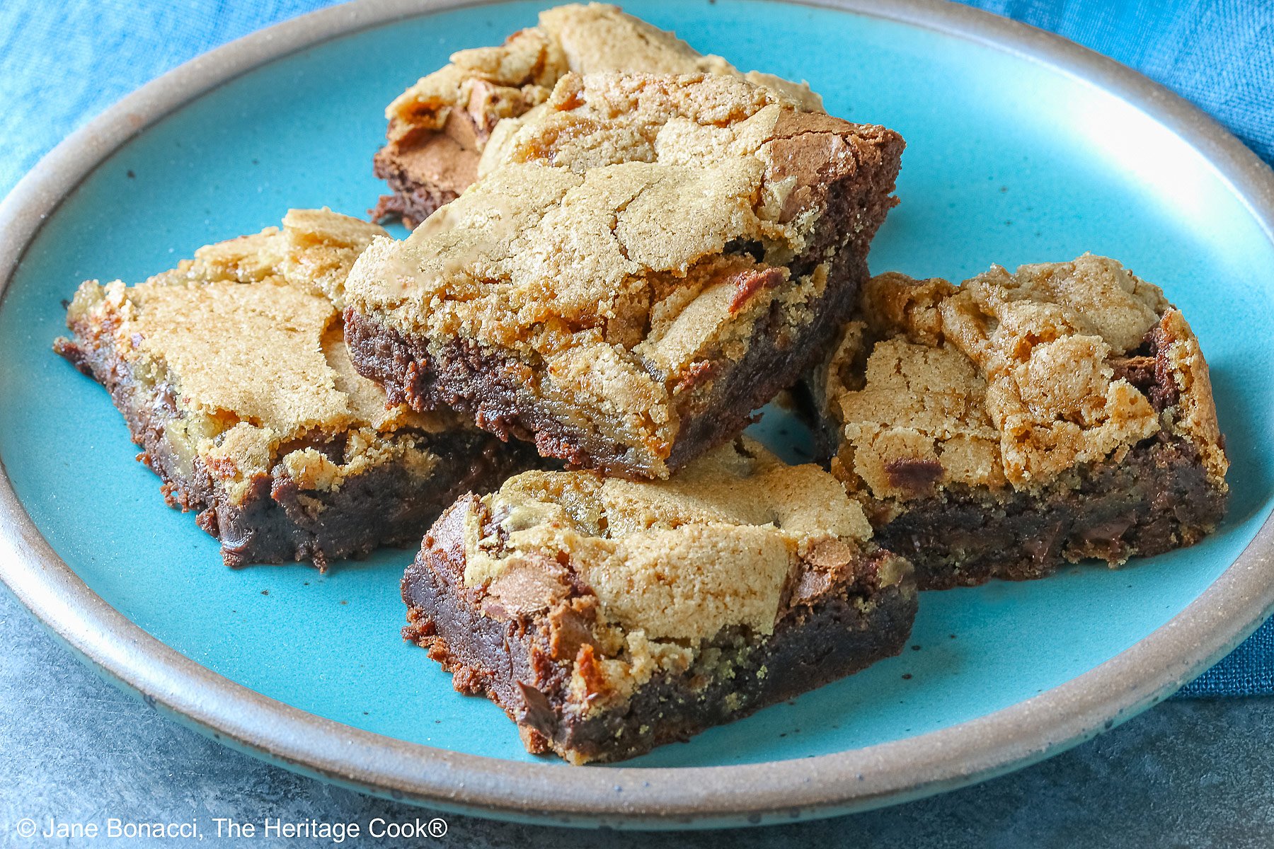 5 stacked Double Chocolate Brookies sitting on a turquoise colored plate with a medium blue cloth behind, on a mottled gray background © 2025 Jane Bonacci, The Heritage Cook.