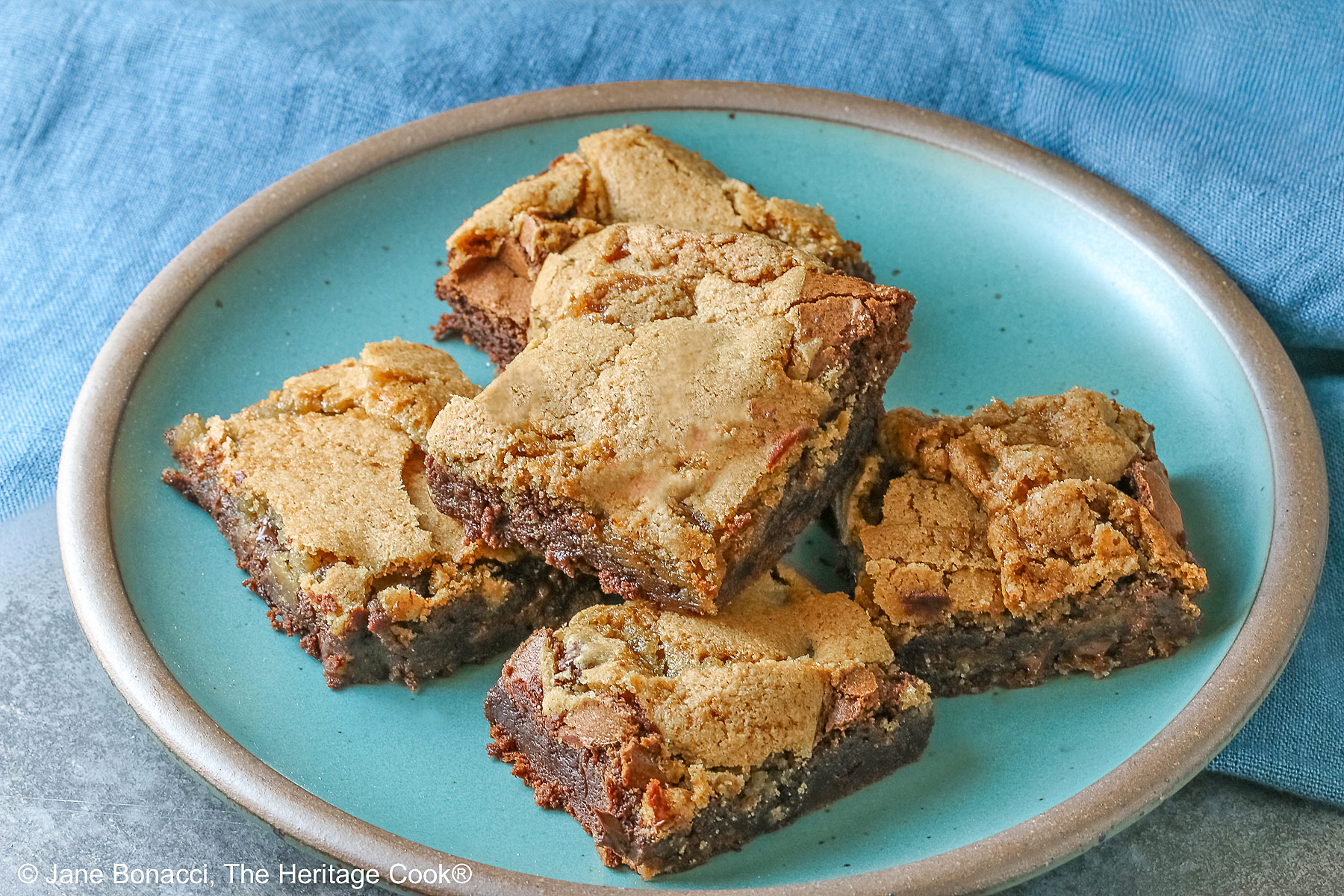5 stacked Double Chocolate Brookies sitting on a turquoise colored plate with a medium blue cloth behind, on a mottled gray background © 2025 Jane Bonacci, The Heritage Cook.