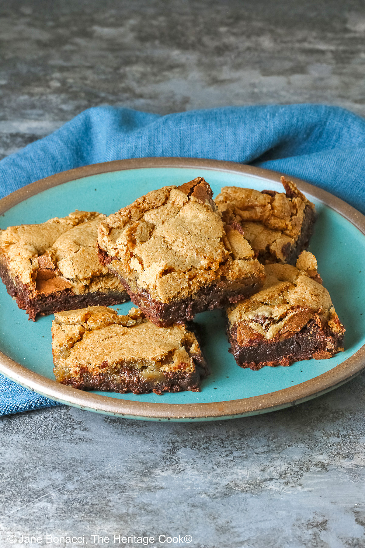 5 stacked Double Chocolate Brookies sitting on a turquoise colored plate with a medium blue cloth behind, on a mottled gray background © 2025 Jane Bonacci, The Heritage Cook.