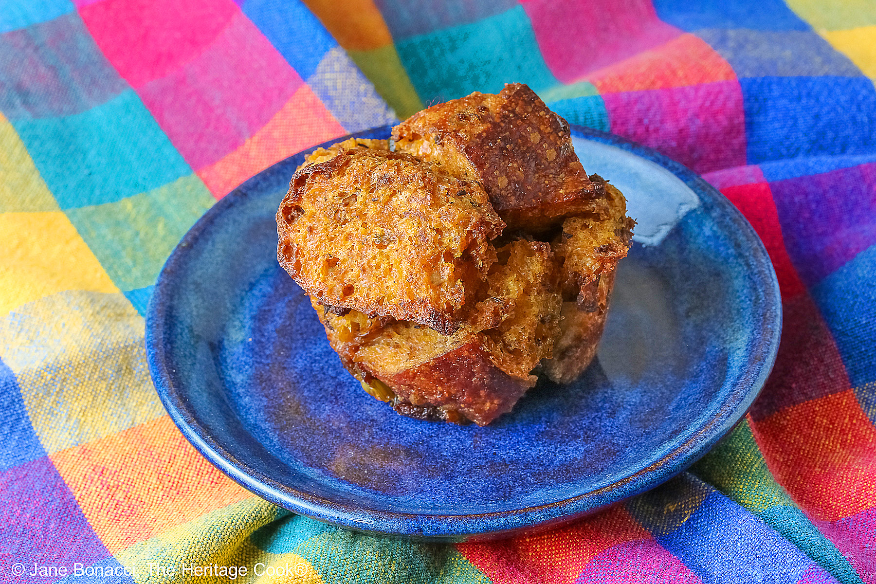 Single Holiday Stuffin Muffin on a handmade blue plate sitting on a brightly colored plaid cloth. 