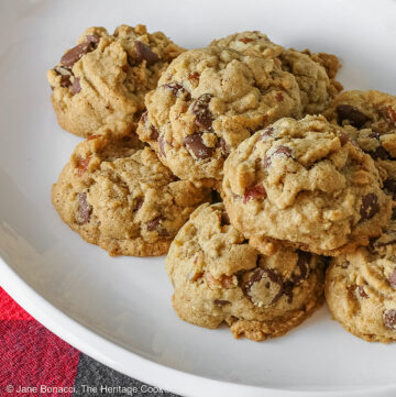 Elongated pile of Bourbon Spiked Chocolate Chip Cookies on a small white oval platter, sitting on a red and black checked buffalo plaid cloth © 2025 Jane Bonacci, The Heritage Cook.