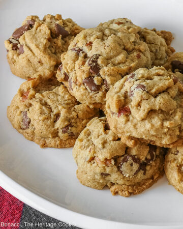 Elongated pile of Bourbon Spiked Chocolate Chip Cookies on a small white oval platter, sitting on a red and black checked buffalo plaid cloth © 2025 Jane Bonacci, The Heritage Cook.