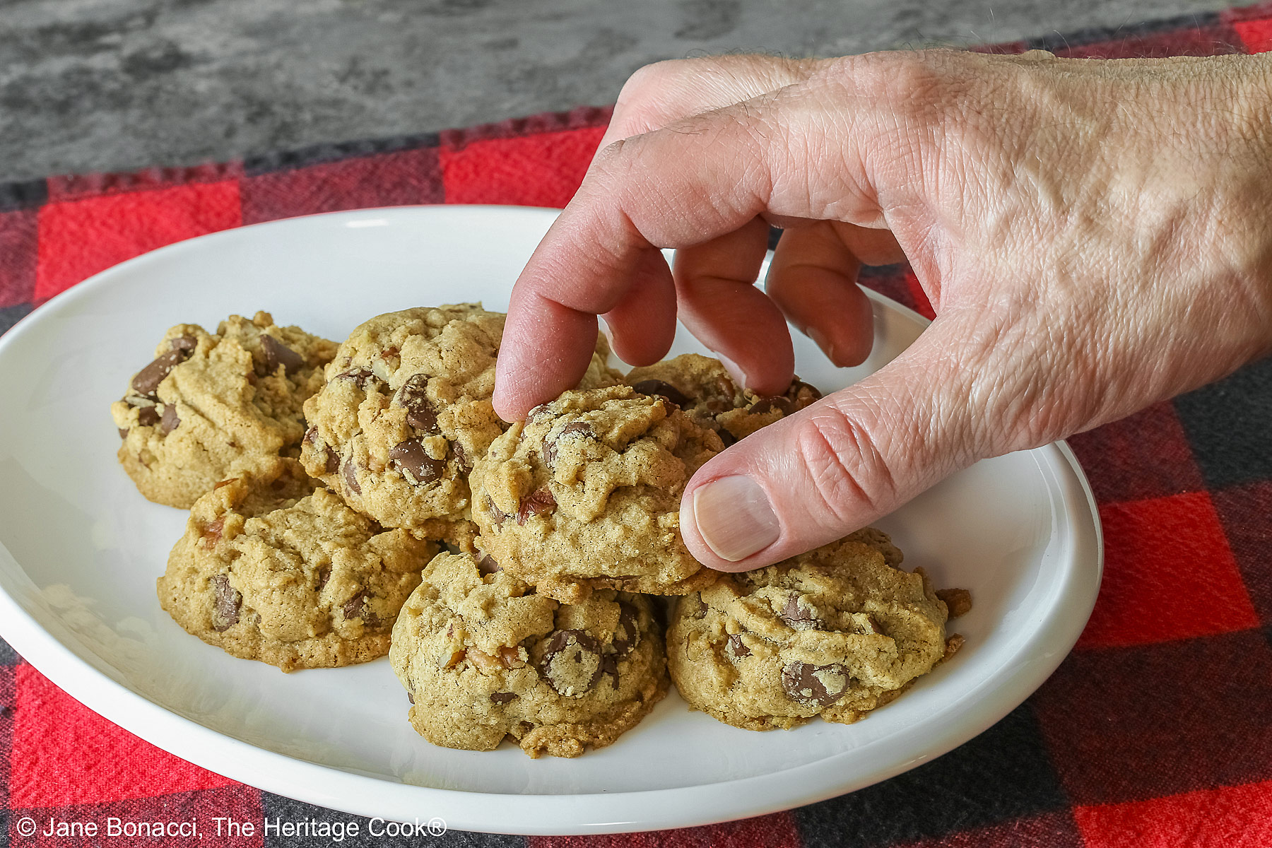 A hand reaching for one of the cookies from the platter. 