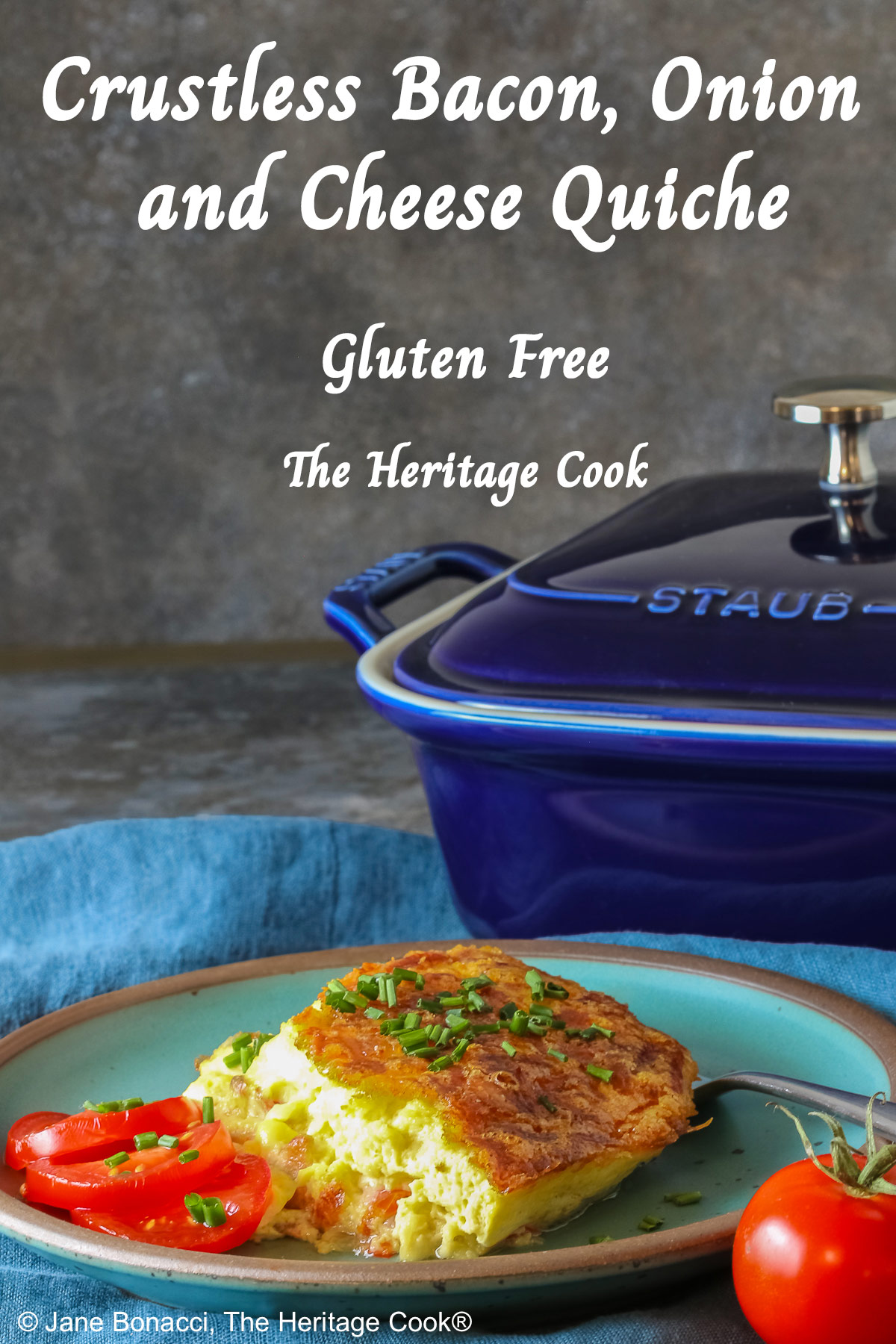 Aqua plate with a square of the crustless quiche with chopped chives on top and 3 tomato slices beside the quiche plus two whole tomatoes next to the plate, sitting on a blue cloth © 2025 Jane Bonacci, The Heritage Cook.