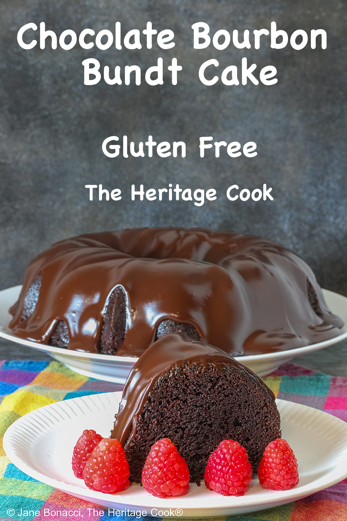 Chocolate Bourbon Bundt Cake on a white plate sitting on a brightly colored plaid cloth, some with a slice with a row of raspberries in front and a few with the whole cake behind © 2026 Jane Bonacci, The Heritage Cook.