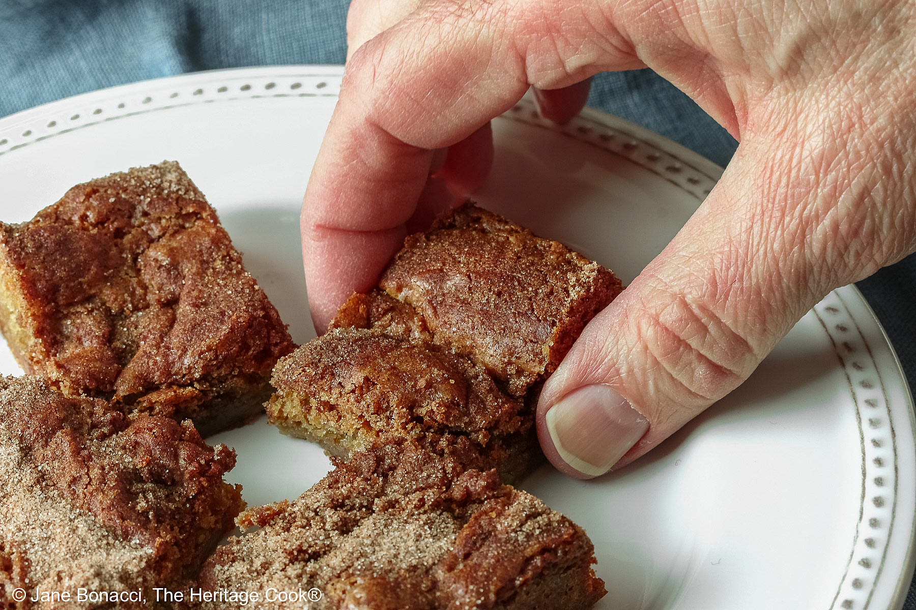 Hand reaching to grab one of the blondies off the plate.