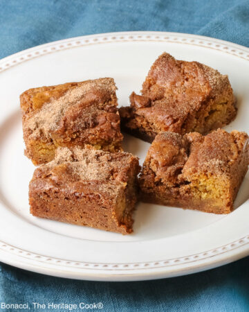 Four Cinnamon Sugar Blondies on a creamy white plate with small beads around the rim, set in a circle and stacks of two each, with a pale blue-teal cloth on a mottled gray background © 2026 Jane Bonacci, The Heritage Cook.