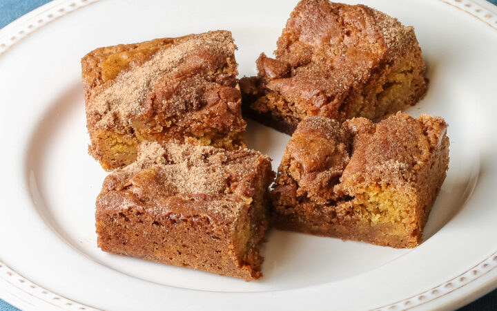 Four Cinnamon Sugar Blondies on a creamy white plate with small beads around the rim, set in a circle and stacks of two each, with a pale blue-teal cloth on a mottled gray background © 2026 Jane Bonacci, The Heritage Cook.