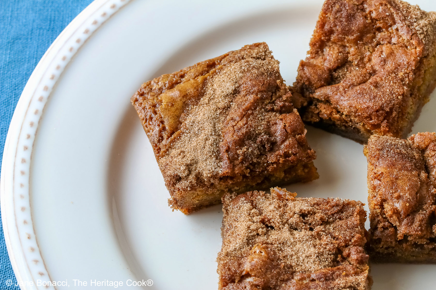 Four Cinnamon Sugar Blondies on a creamy white plate with small beads around the rim, set in a circle and stacks of two each, with a pale blue-teal cloth on a mottled gray background © 2026 Jane Bonacci, The Heritage Cook.