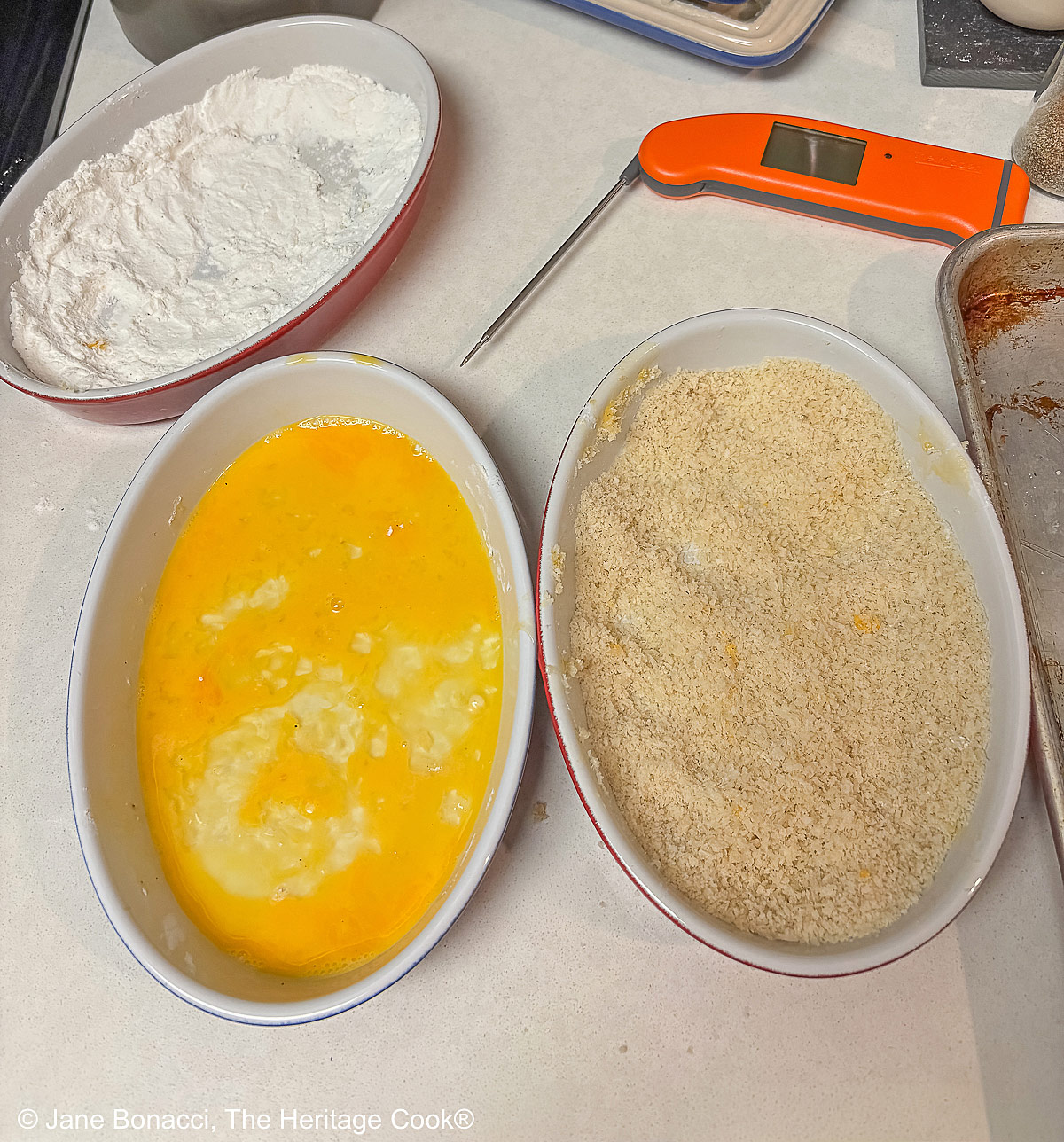 A breading station with 3 dishes, one for flour, one for beaten eggs, and the last for seasoned panko breadcrumbs, plus an instant read thermometer.