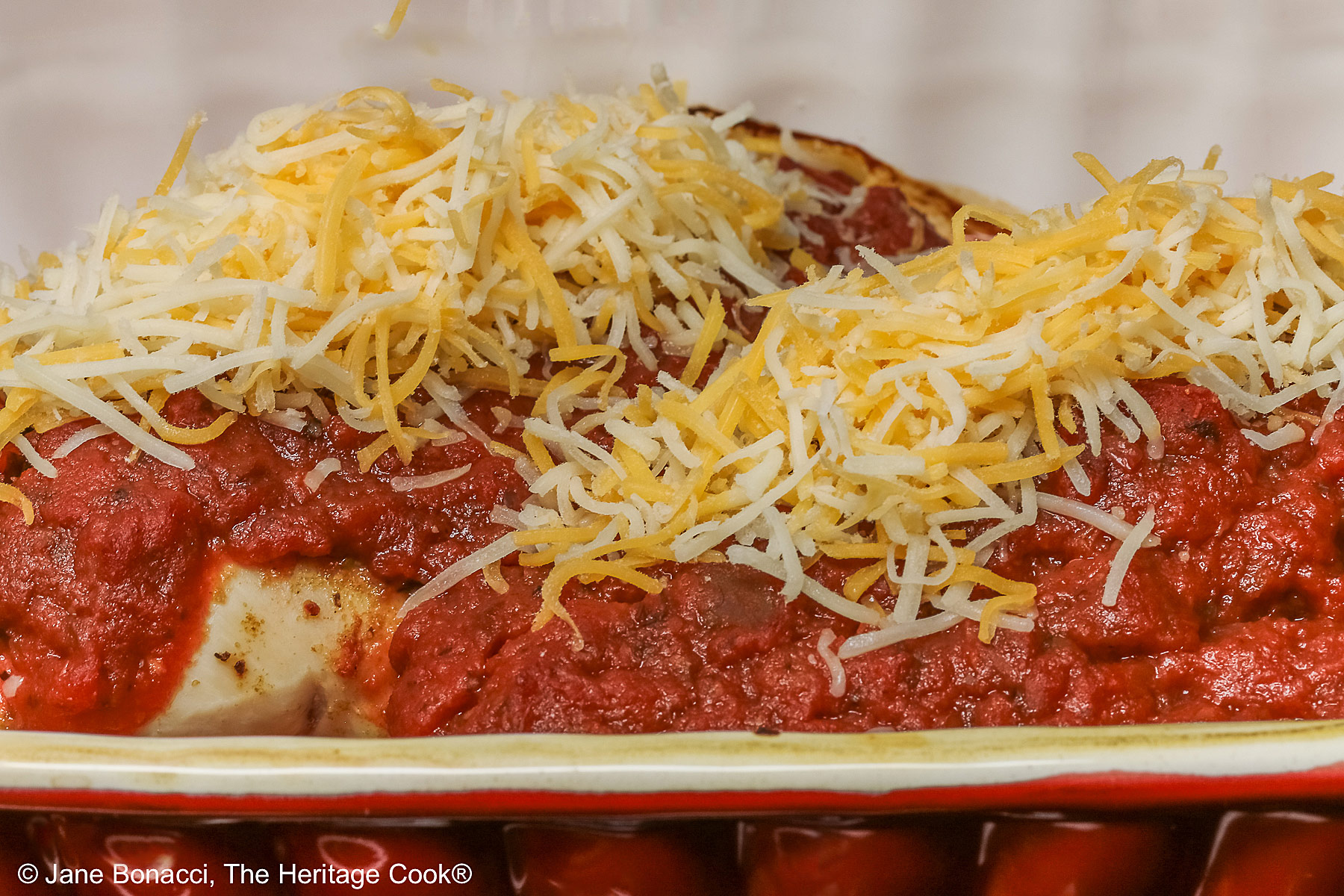 Two partially baked chicken breasts topped with shredded cheese before final baking.