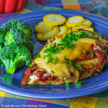 Varying angles of a salsa and melted cheese covered chicken breast with a sprinkling of chives on a blue plate surrounded by broccoli, squash coins, and lime slices, sitting on a brightly colored square cloths © 2026 Jane Bonacci, The Heritage Cook.