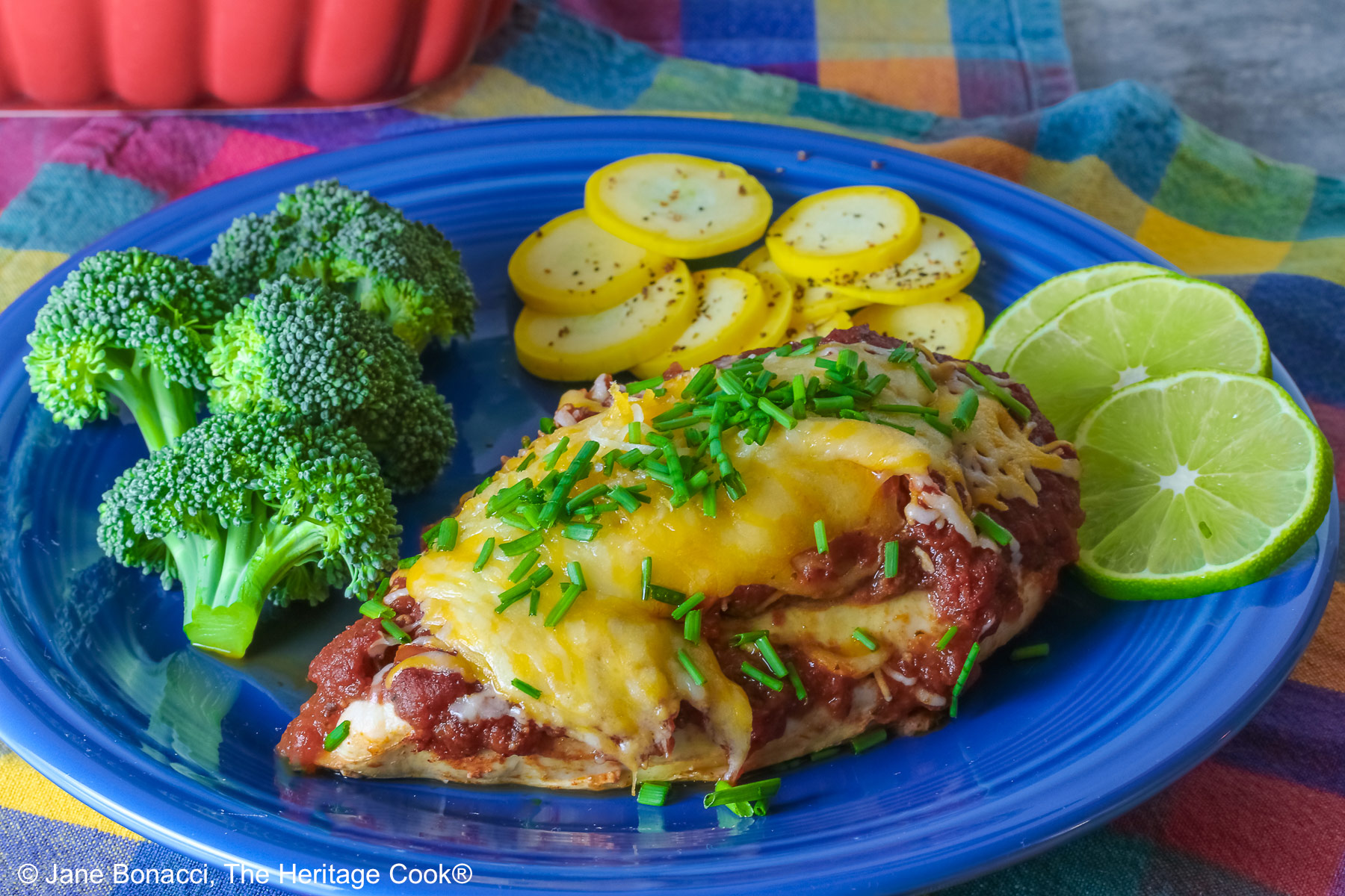Varying angles of a salsa and melted cheese covered chicken breast with a sprinkling of chives on a blue plate surrounded by broccoli, squash coins, and lime slices, sitting on a brightly colored square cloths © 2026 Jane Bonacci, The Heritage Cook.