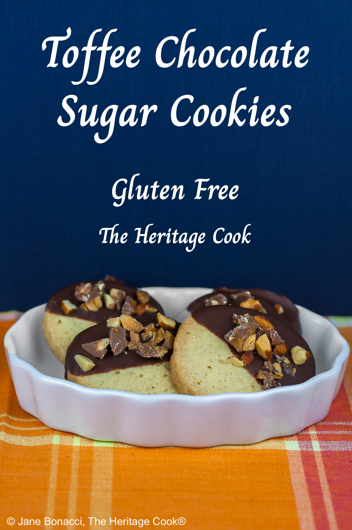 4 chocolate dipped sugar cookies topped with chopped toffee almond pieces, assembled in a white brulee dish sitting on a pink and orange plaid cloth © 2026 Jane Bonacci, The Heritage Cook.