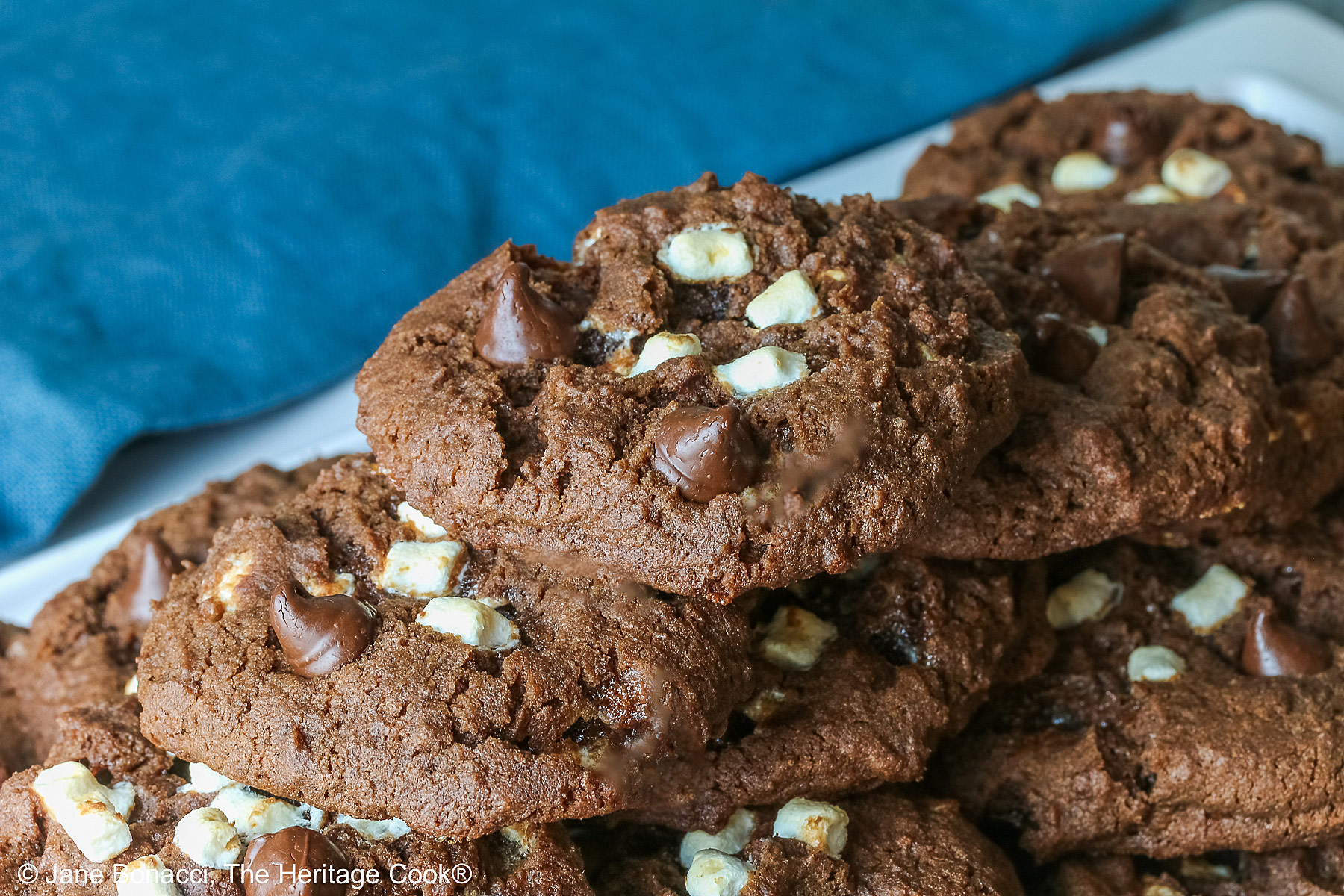Hot Cocoa Cookies stacked in a wide pyramid shape, each cookie topped with extra micro mini marshmallow bits and chocolate chips, a big pile of dark brown chocolate cookies © 2026 Jane Bonacci, The Heritage Cook.