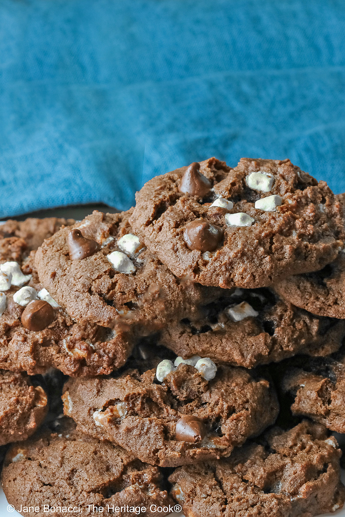 Hot Cocoa Cookies stacked in a wide pyramid shape, each cookie topped with extra micro mini marshmallow bits and chocolate chips, a big pile of dark brown chocolate cookies © 2026 Jane Bonacci, The Heritage Cook.