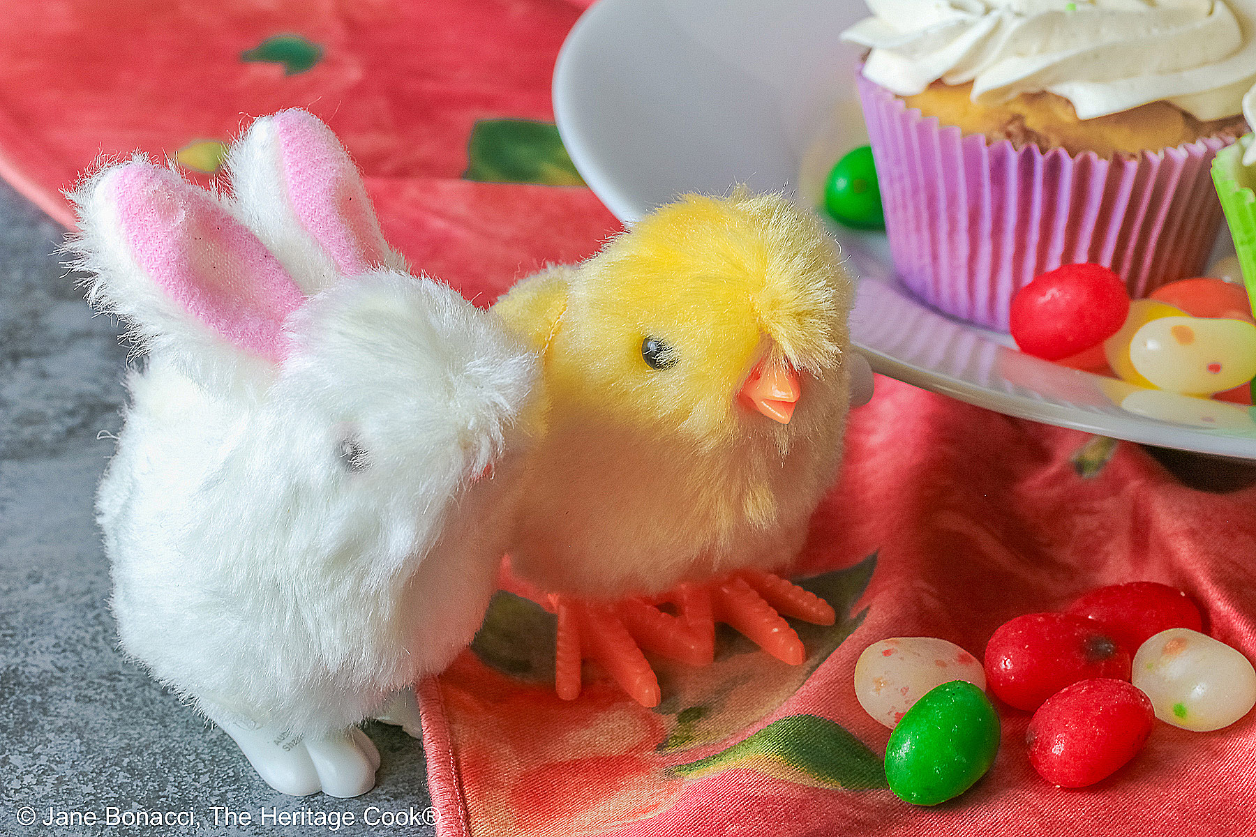 Mini stuffed white bunny with pink ears and yellow chick next to the plate of cupcakes.