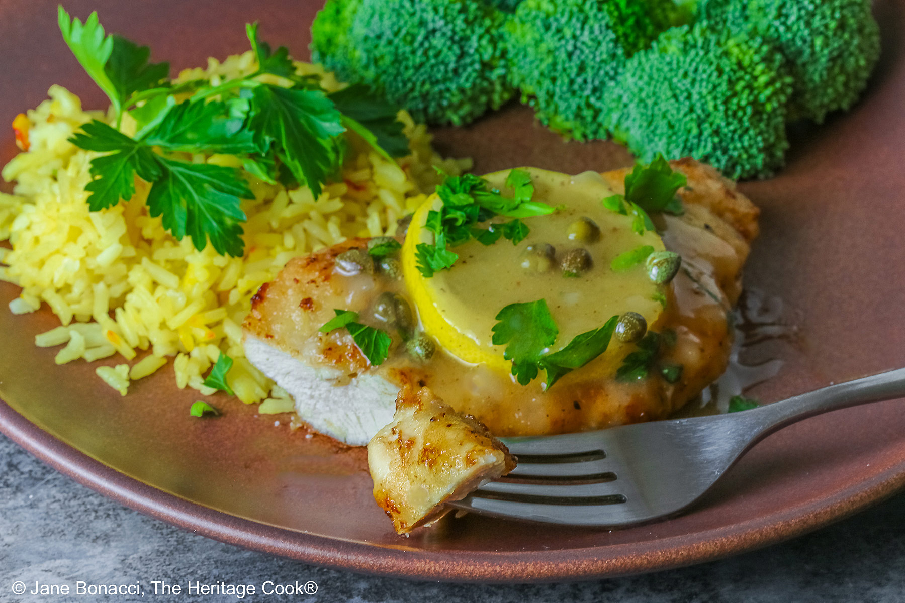 A bite on the fork in front of the chicken with sauce, rice, and broccoli.