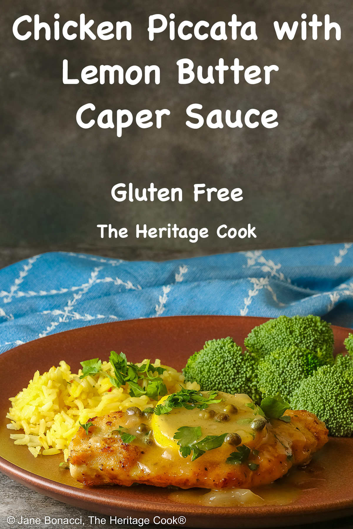Golden brown chicken cutlet with a lemon slice on top, drizzled with butter-lemon-caper piccata sauce, sprinkled with chopped parsley served with yellow saffron rice and fresh broccoli all on a red’ish brown plate with a blue cloth behind © 2026 Jane Bonacci, The Heritage Cook.