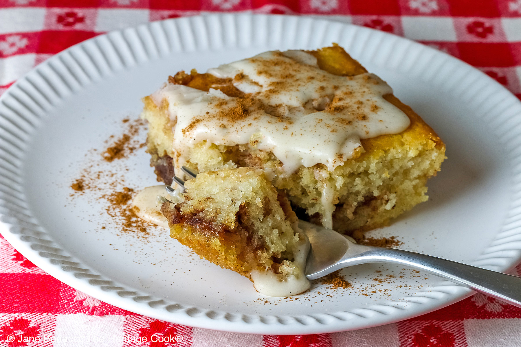 Bite of the cake on a fork in front a slice of the Cinnamon Roll Cake © 2026 Jane Bonacci, The Heritage Cook.