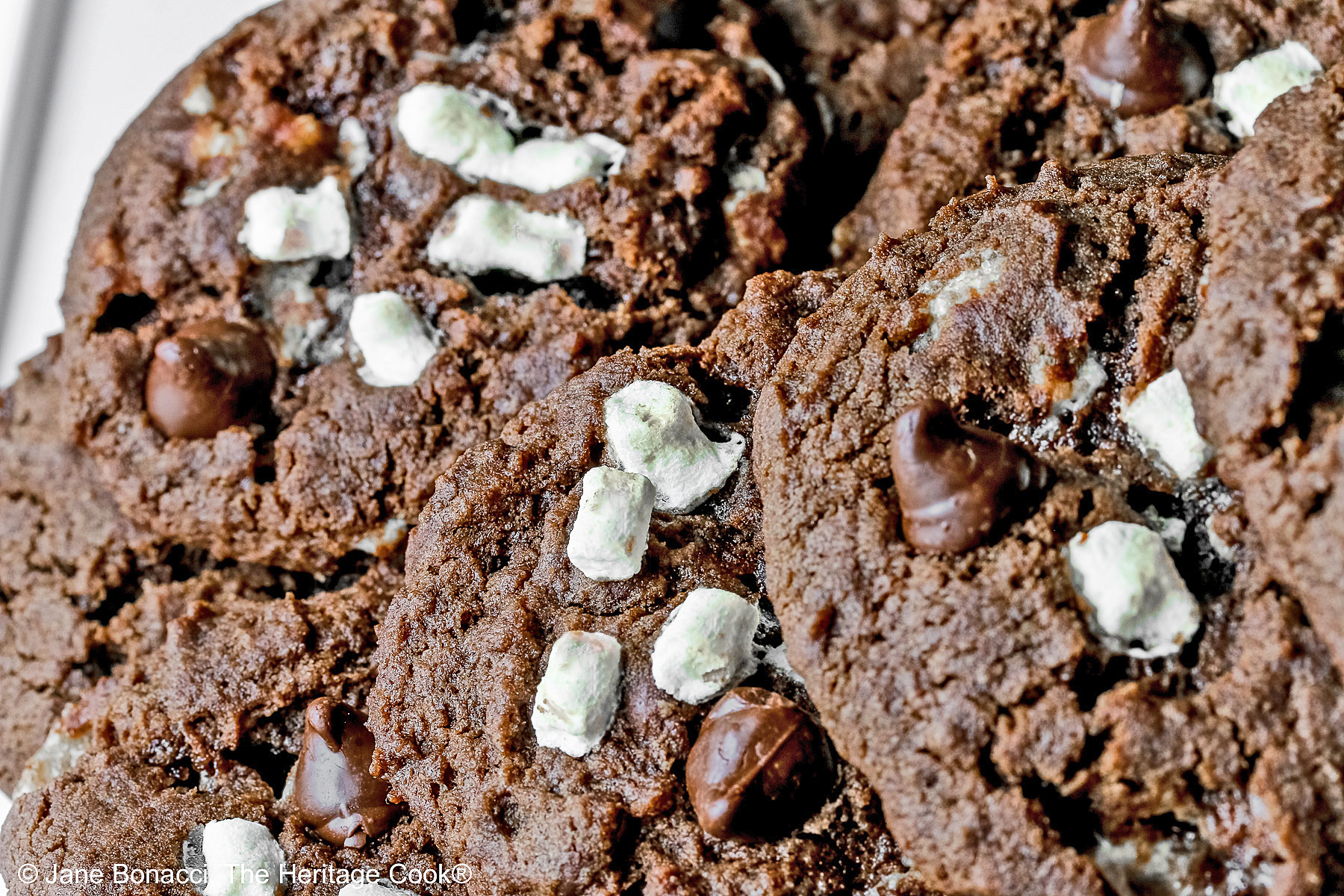 Hot Cocoa Cookies stacked in a wide pyramid shape, each cookie topped with extra micro mini marshmallow bits and chocolate chips, a big pile of dark brown chocolate cookies © 2026 Jane Bonacci, The Heritage Cook.
