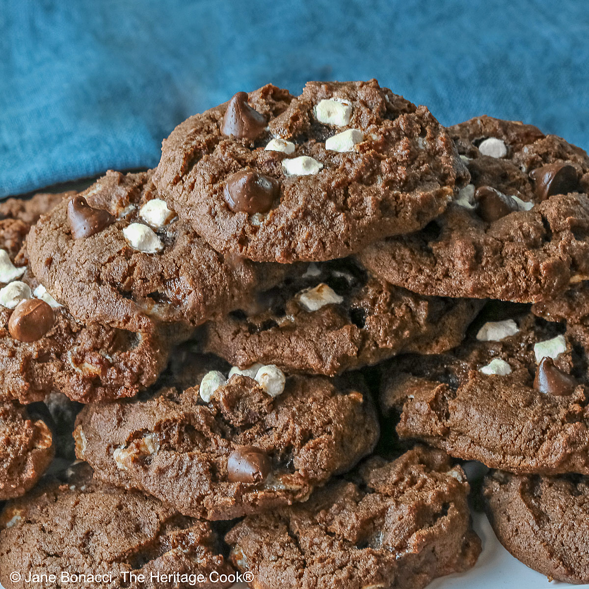 Hot Cocoa Cookies stacked in a wide pyramid shape, each cookie topped with extra micro mini marshmallow bits and chocolate chips, a big pile of dark brown chocolate cookies © 2026 Jane Bonacci, The Heritage Cook.