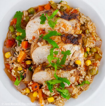 Colorful rice and vegetables with slices of chicken breast laid on top and sprinkled with chopped cilantro/parsley in a white bowl with a wide rim © 2026 Jane Bonacci, The Heritage Cook.