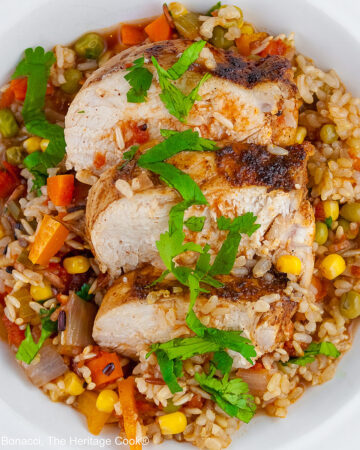 Colorful rice and vegetables with slices of chicken breast laid on top and sprinkled with chopped cilantro/parsley in a white bowl with a wide rim © 2026 Jane Bonacci, The Heritage Cook.