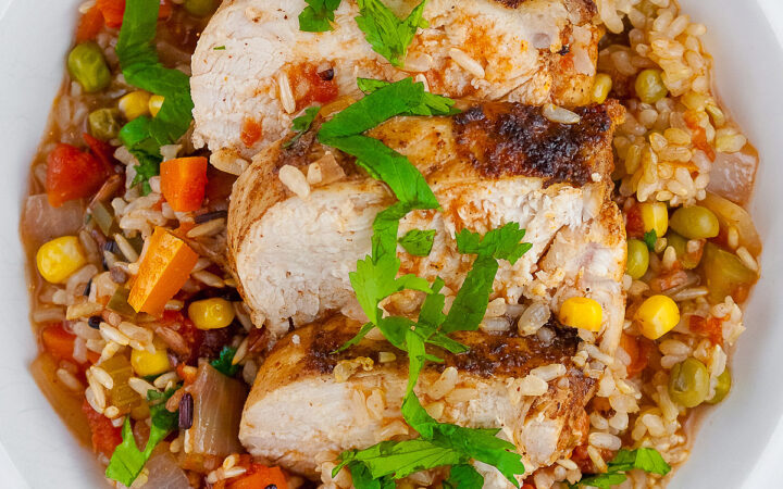 Colorful rice and vegetables with slices of chicken breast laid on top and sprinkled with chopped cilantro/parsley in a white bowl with a wide rim © 2026 Jane Bonacci, The Heritage Cook.