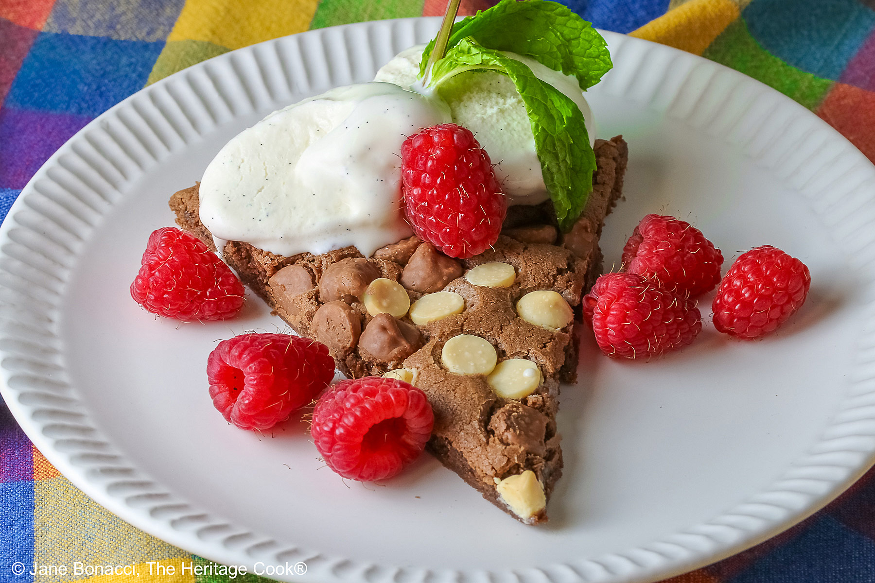 A wedge of the 10-inch (25cm) round Triple Chocolate Jumbo Cookie topped with scoops of vanilla ice cream, fresh red raspberries, and a sprig of mint © 2026 Jane Bonacci, The Heritage Cook.