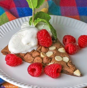 A wedge of the 10-inch (25cm) round Triple Chocolate Jumbo Cookie topped with scoops of vanilla ice cream, fresh red raspberries, and a sprig of mint © 2026 Jane Bonacci, The Heritage Cook.