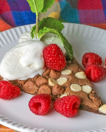 A wedge of the 10-inch (25cm) round Triple Chocolate Jumbo Cookie topped with scoops of vanilla ice cream, fresh red raspberries, and a sprig of mint © 2026 Jane Bonacci, The Heritage Cook.