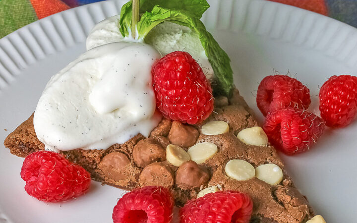 A wedge of the 10-inch (25cm) round Triple Chocolate Jumbo Cookie topped with scoops of vanilla ice cream, fresh red raspberries, and a sprig of mint © 2026 Jane Bonacci, The Heritage Cook.
