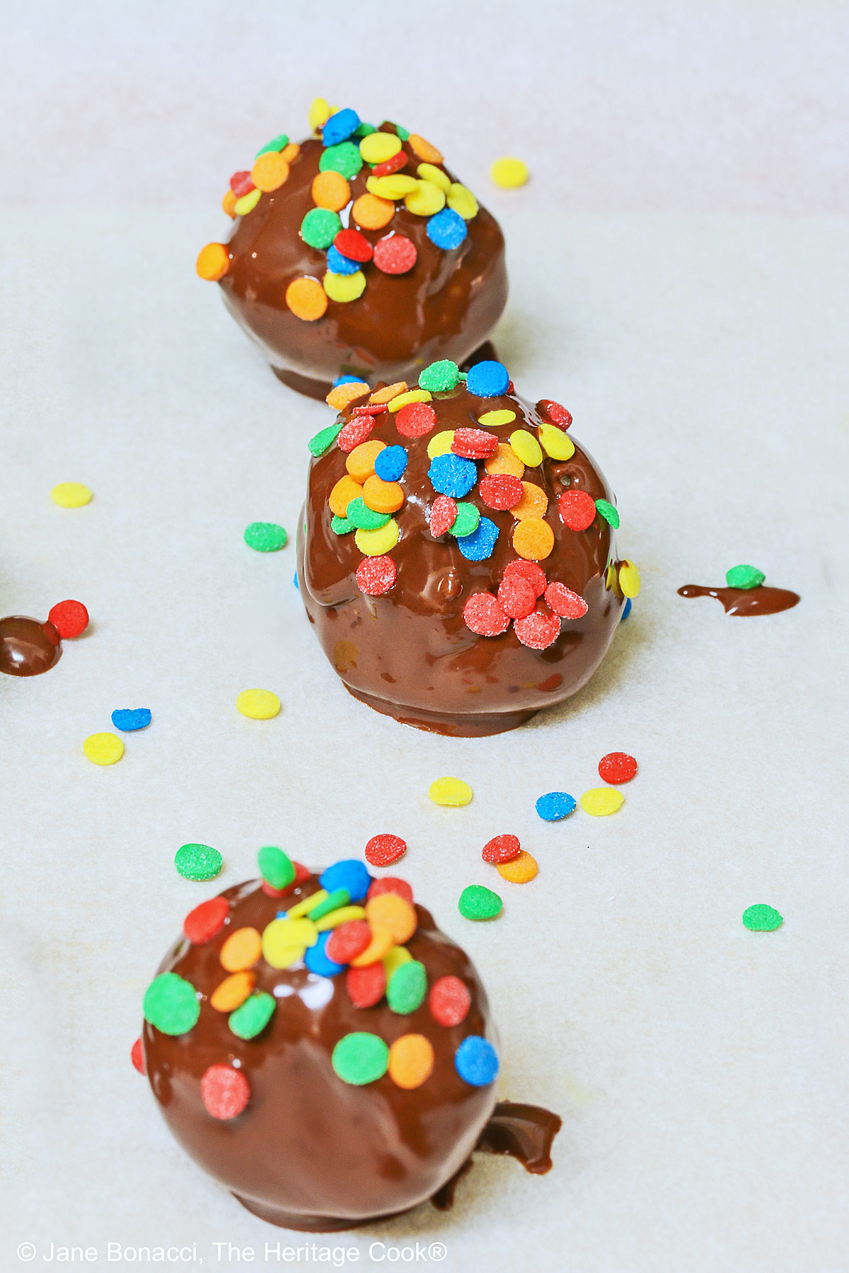 3 freshly dipped truffles with confetti candy on top, sitting on the parchment paper.