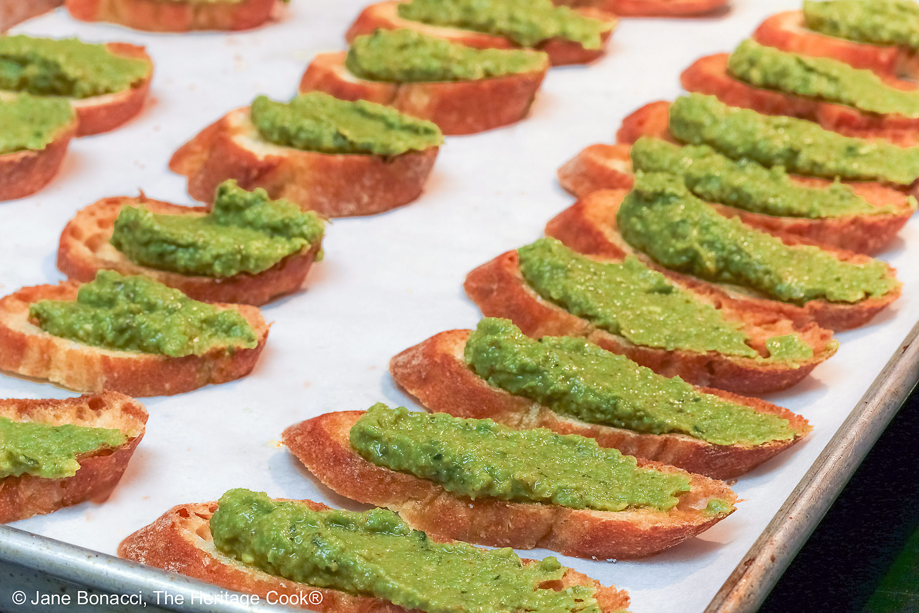Baking sheet pan filled with lines of pea puree covered crostini.
