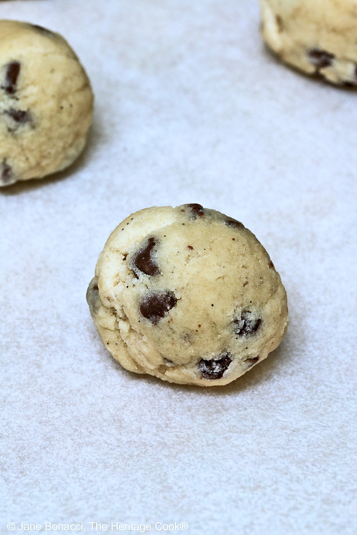 3 un-dipped cookie dough truffles on parchment paper.