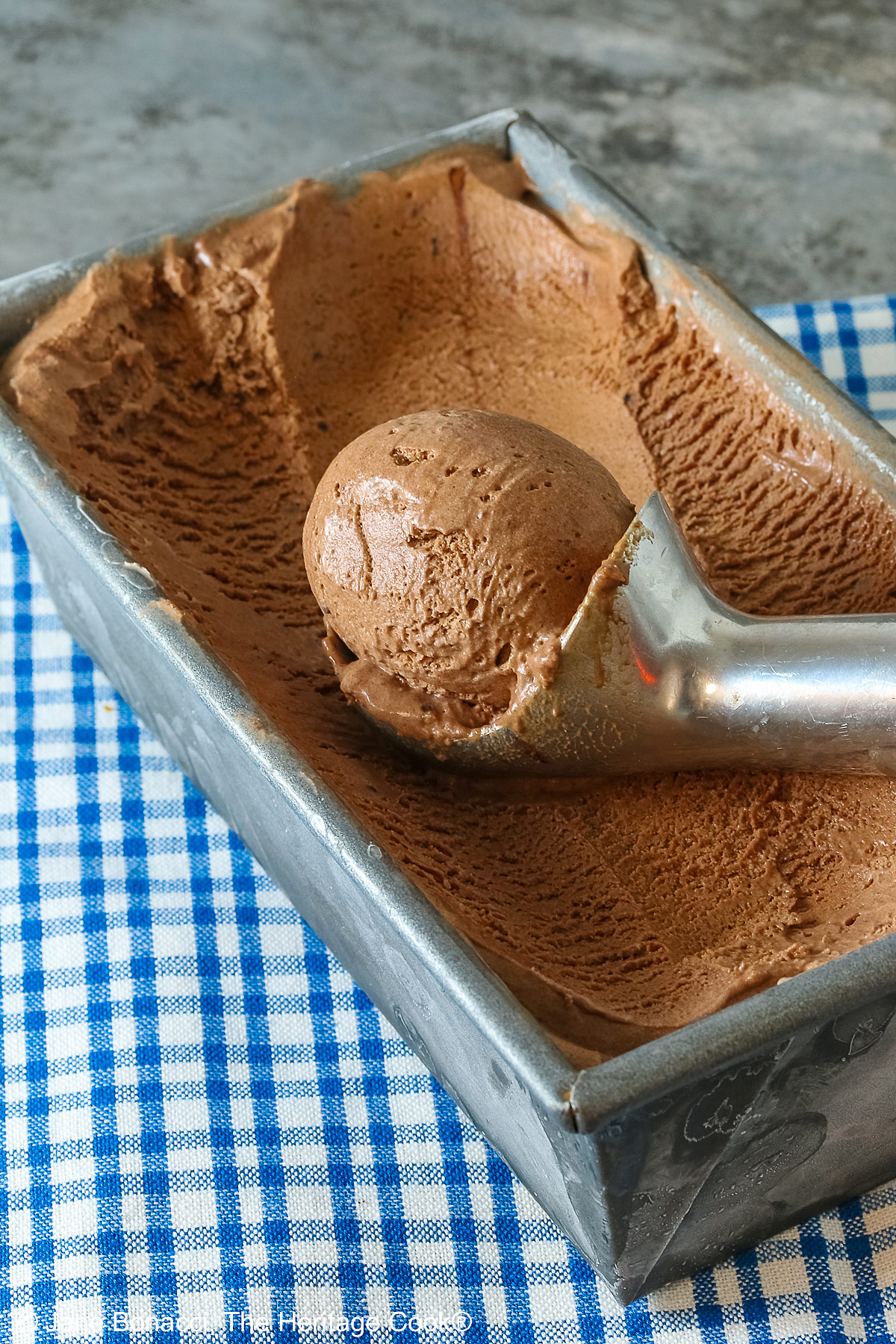 A ball of ice cream in the scoop sitting in the pan of dark chocolate ice cream.
