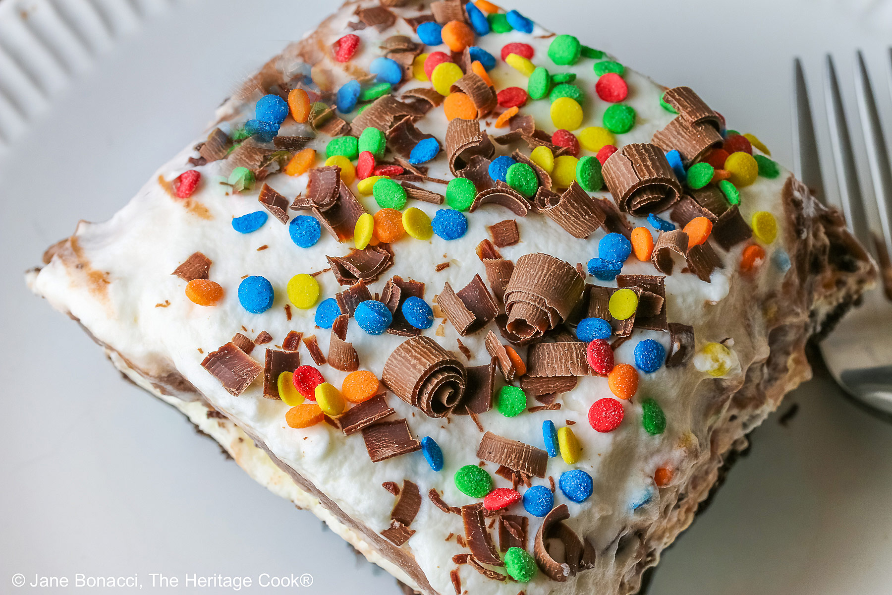 The decorated top of a slice, covered with shaved chocolate and rainbow sprinkles for a fun and festive dessert.