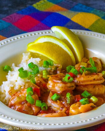 Pale yellow bowl filled with long grain rice topped with New Orleans Shrimp Creole topped with perfectly cooked shrimp, sprinkled with sliced green onions and minced red bell peppers, with 3 wedges of fresh lemon © 2026 Jane Bonacci, The Heritage Cook.