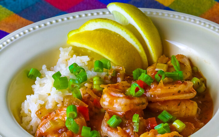 Pale yellow bowl filled with long grain rice topped with New Orleans Shrimp Creole topped with perfectly cooked shrimp, sprinkled with sliced green onions and minced red bell peppers, with 3 wedges of fresh lemon © 2026 Jane Bonacci, The Heritage Cook.