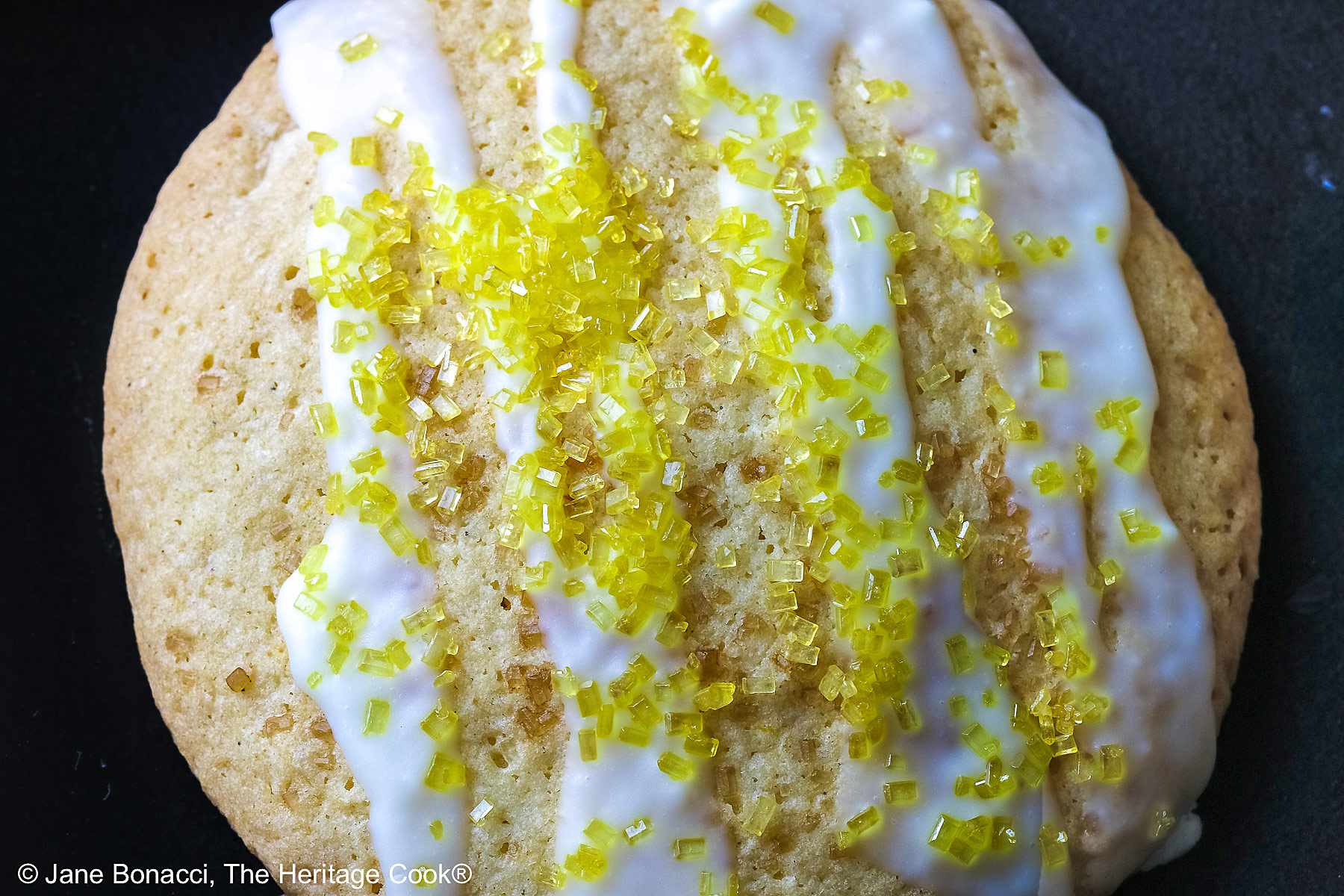 Tight close up of a single cookie with white chocolate drizzle and sprinkling of yellow sugar on top.